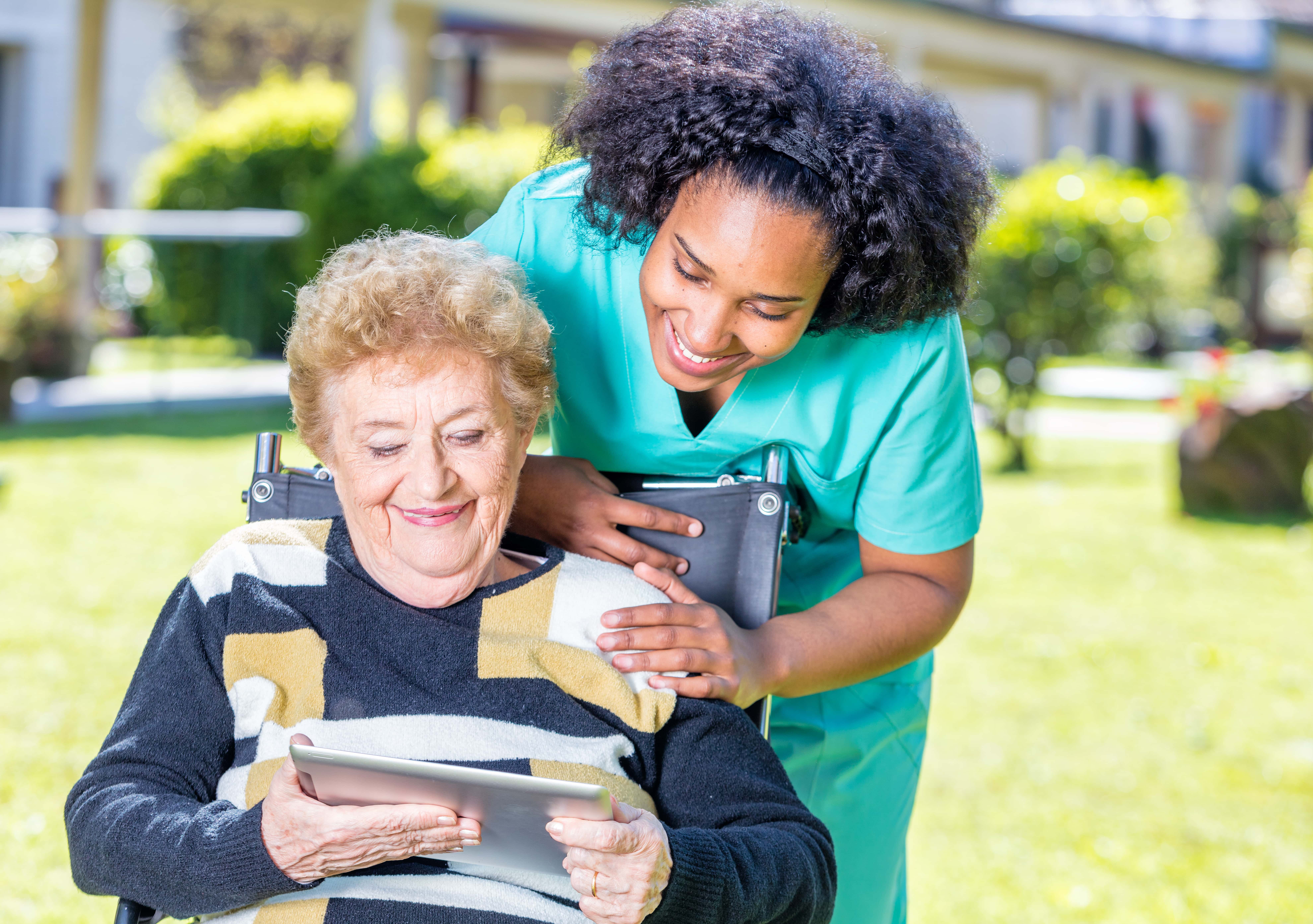 Nurse explaining tablet use to elder woman on wheelchair.